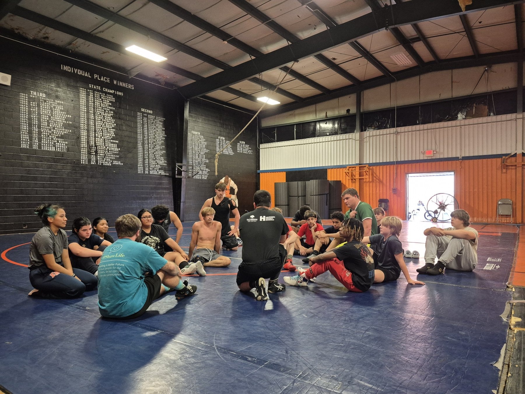 WRESTLERS AND COACHES GATHERED ON THE MAT